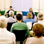 Rows of adults watching two young violinists at a school concert