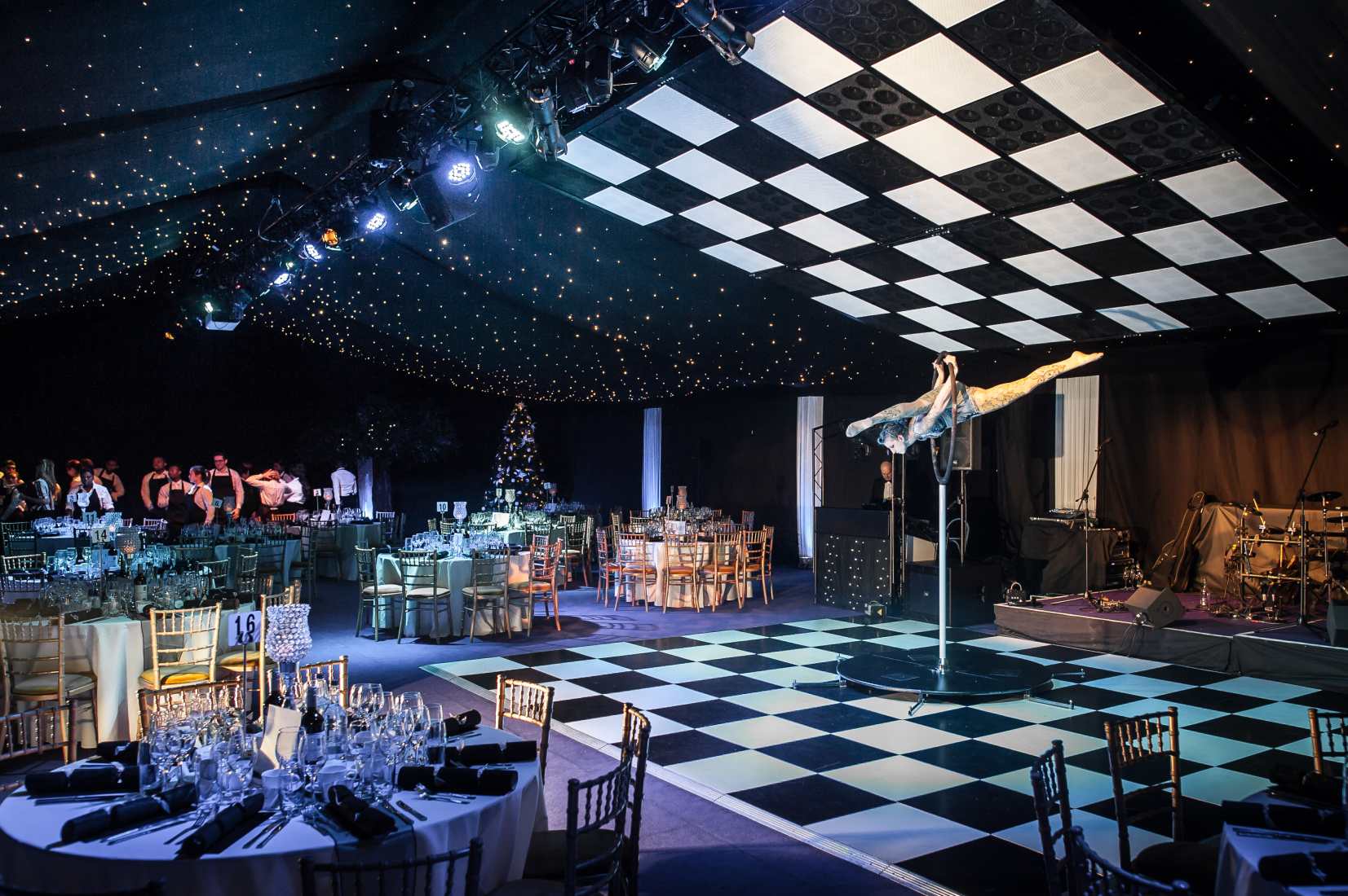 A function room dressed spectaculalry in black and white, with a black and white checked dance floor, a stage, band equipment and an acrobatic performer.